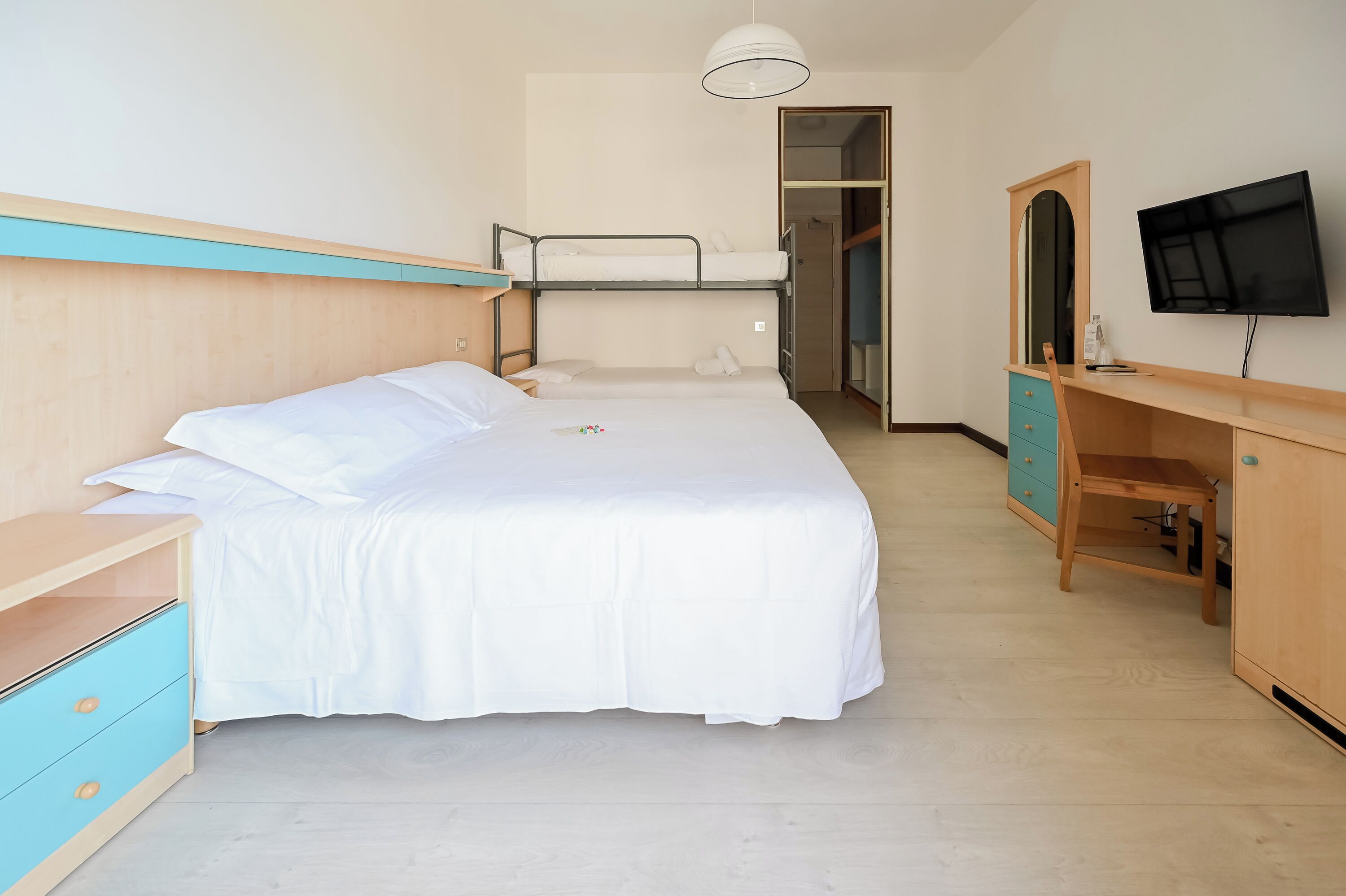 A hotel room with a bunk bed, a desk with a mirror, a television, and a wardrobe.