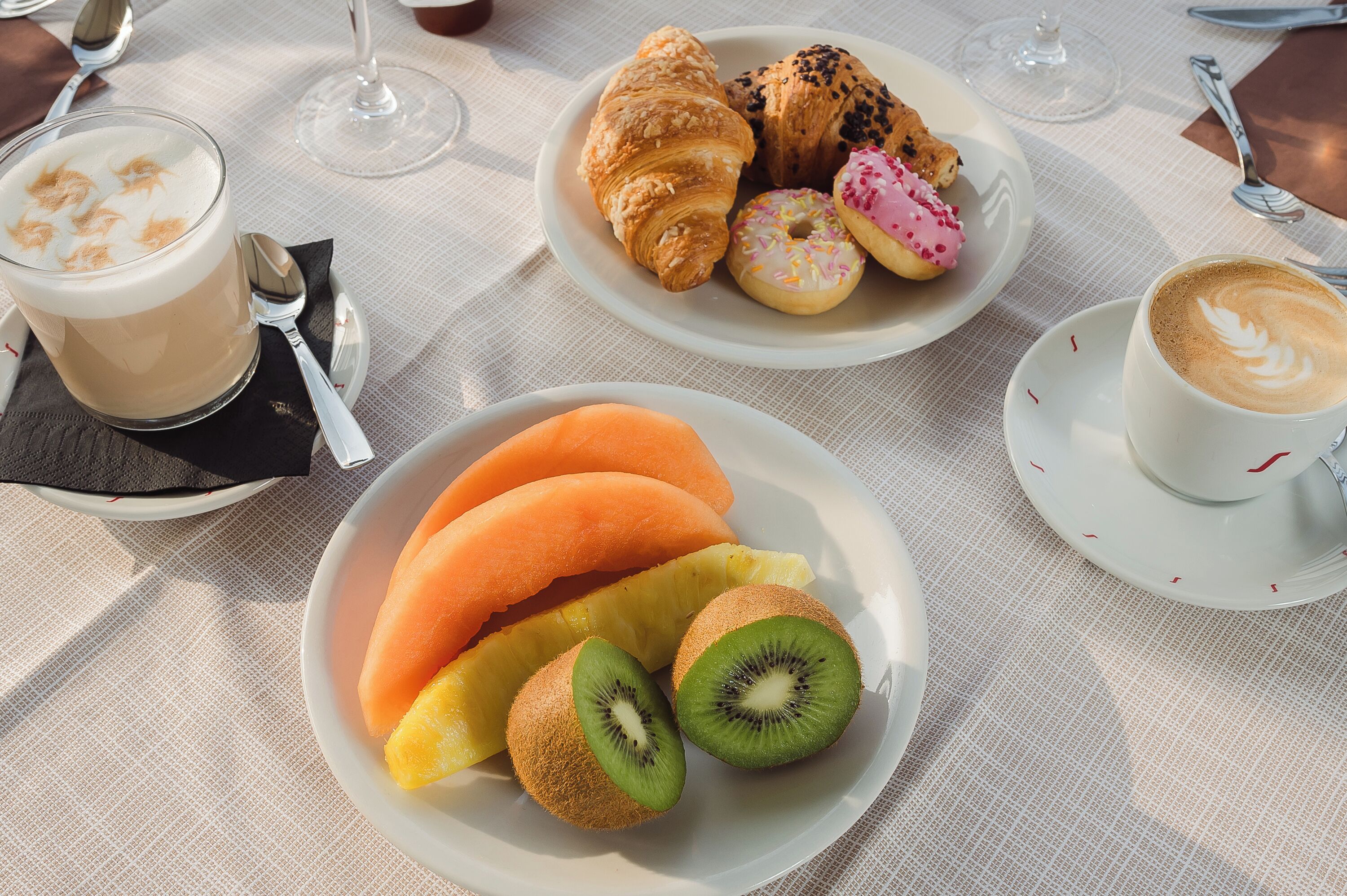 A table set with croissants, pastries, a glass of coffee, and a bowl of fruit.