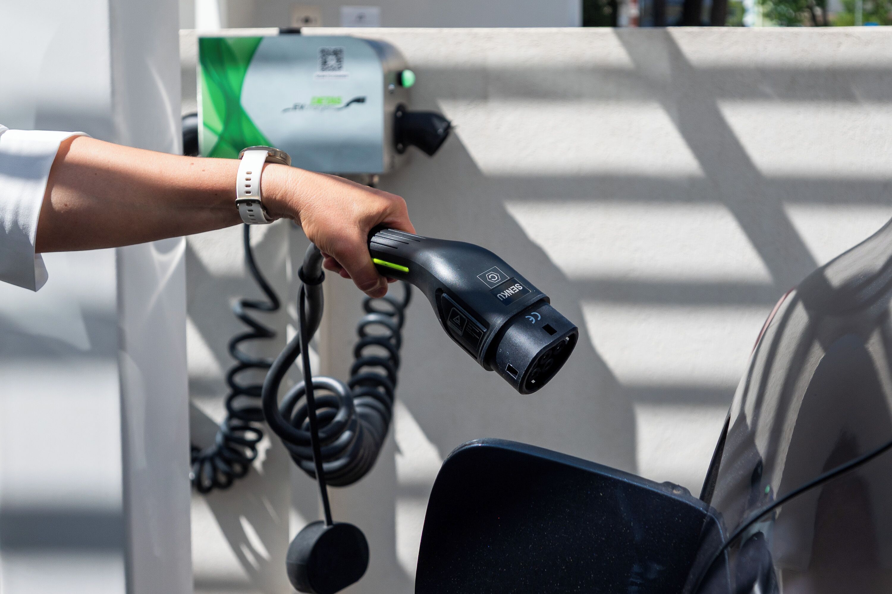 A hand holding a charging cable at an electric vehicle charging station.