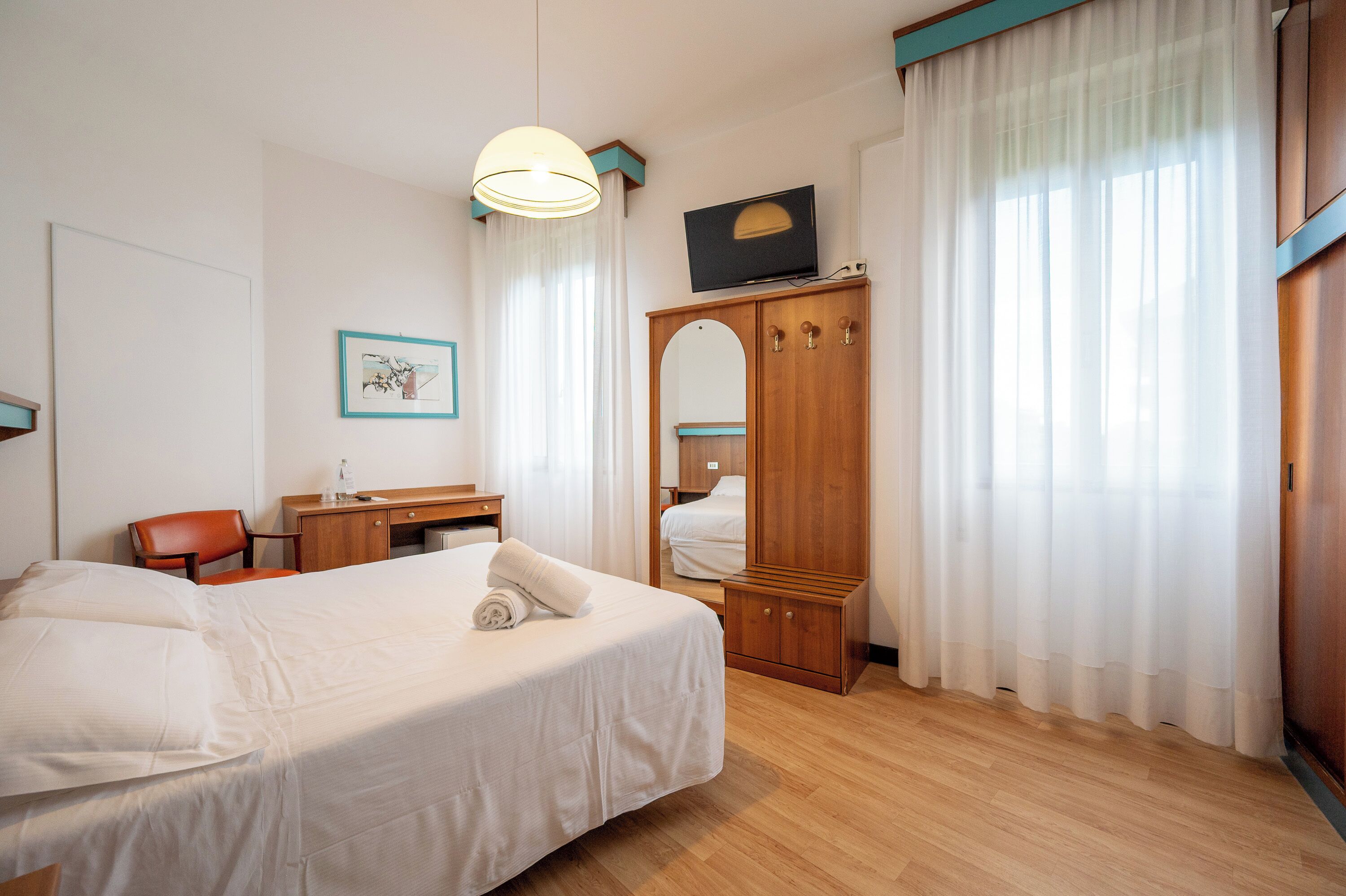 Een hotelkamer met een bed, een bureau, een stoel, een kledingkast en een televisie.
