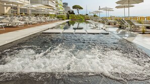 Une piscine dotée de jets d’eau, entourée de chaises longues et de parasols, avec un bâtiment en arrière-plan.