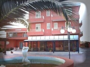 A pink building with balconies and a fountain. - Cordial Hotel (Comiso)