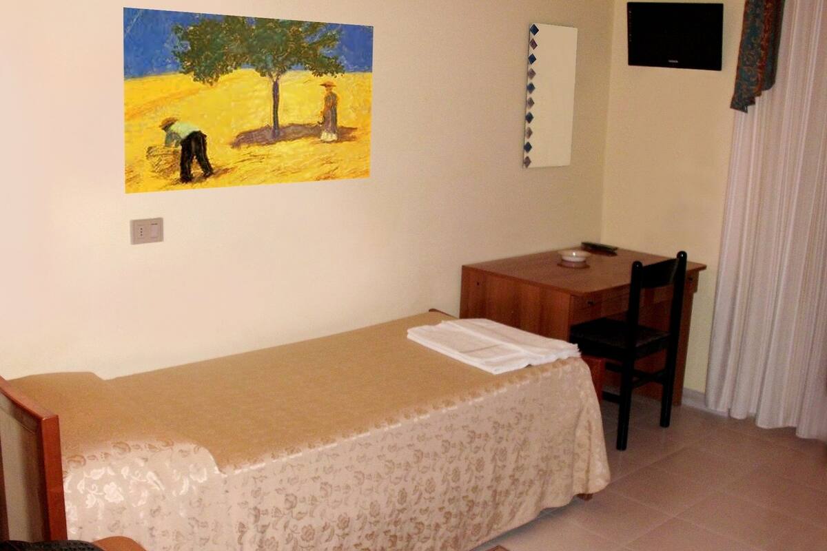 Un dormitorio pequeño y ordenado con una cama individual, un escritorio, una silla, un teléfono y un cuadro en la pared.