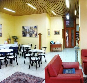 Un espace repas avec des tables et des chaises rondes, un canapé rouge et un plafond en bois doté d’un éclairage encastré.