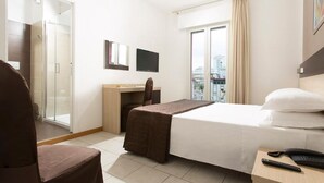 A hotel room with a bed, a desk, a chair, a TV, and a view of the city. - Hotel Gardenia (Jesolo)