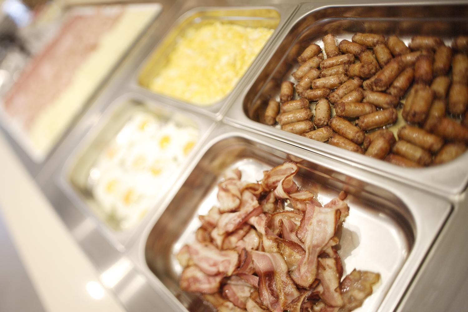A buffet with various food options including sausages, bacon, and scrambled eggs.