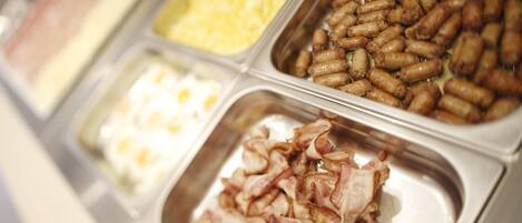 A buffet with various food options including sausages, bacon, and scrambled eggs.