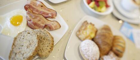 A breakfast buffet with various dishes including eggs, bacon, pastries, and a fruit bowl.