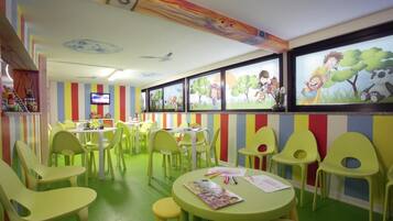 A children's play area with colorful striped walls, green and yellow chairs, and a television on the wall.