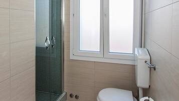 Ein kleines Badezimmer mit einer Duschkabine, einer Toilette und einem Fenster über der Toilette.