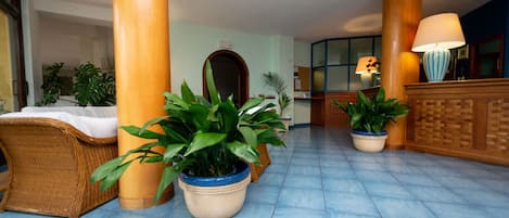 Un vestíbulo con suelo de baldosas azules, muebles de mimbre y plantas en macetas.