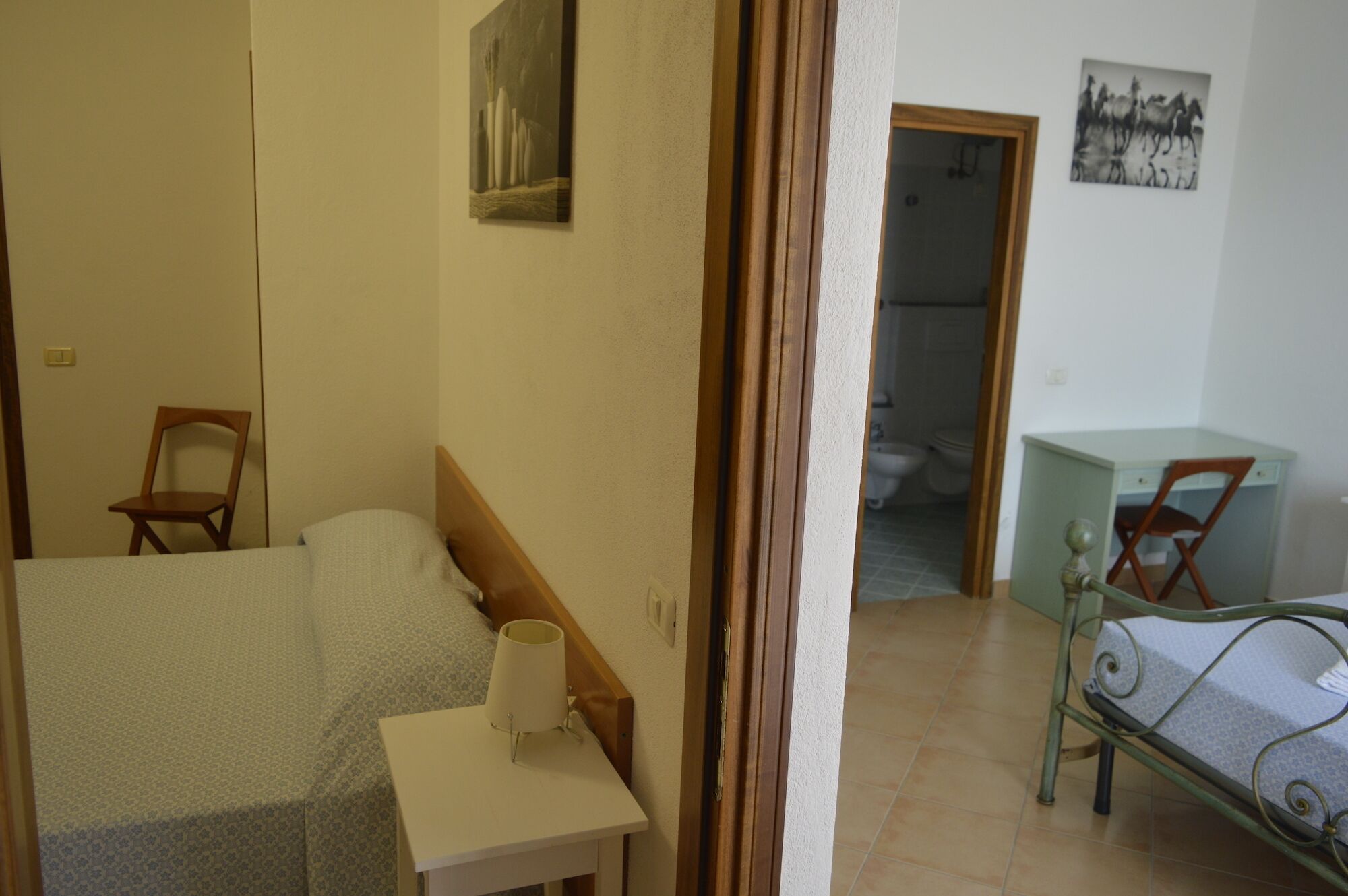 A bedroom with a bed, a chair, a desk, and a bathroom visible through an open door.