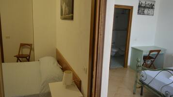 A bedroom with a bed, a chair, a desk, and a bathroom visible through an open door.