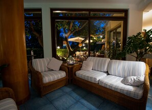 A wicker sofa with striped cushions in a well-lit outdoor area with a view of trees and a patio.