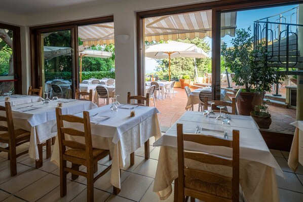 Un área de comedor al aire libre con mesas, sillas, sombrillas grandes y plantas en macetas.