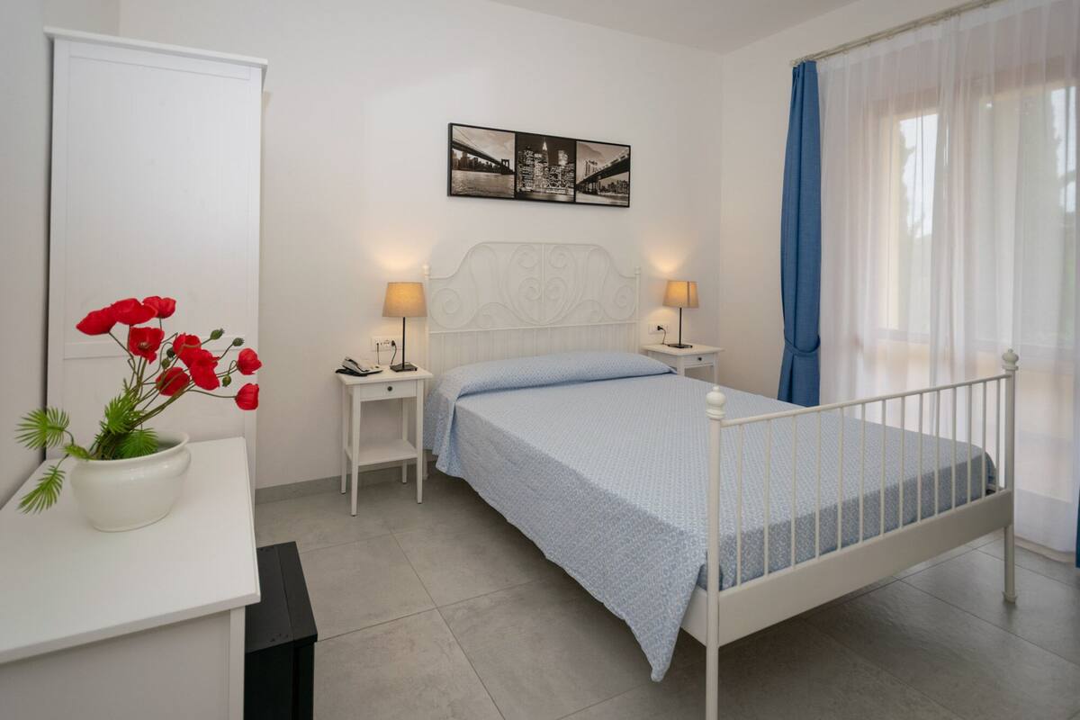 A bedroom with a bed, bedside tables, a lamp, a picture on the wall, and a window with curtains.