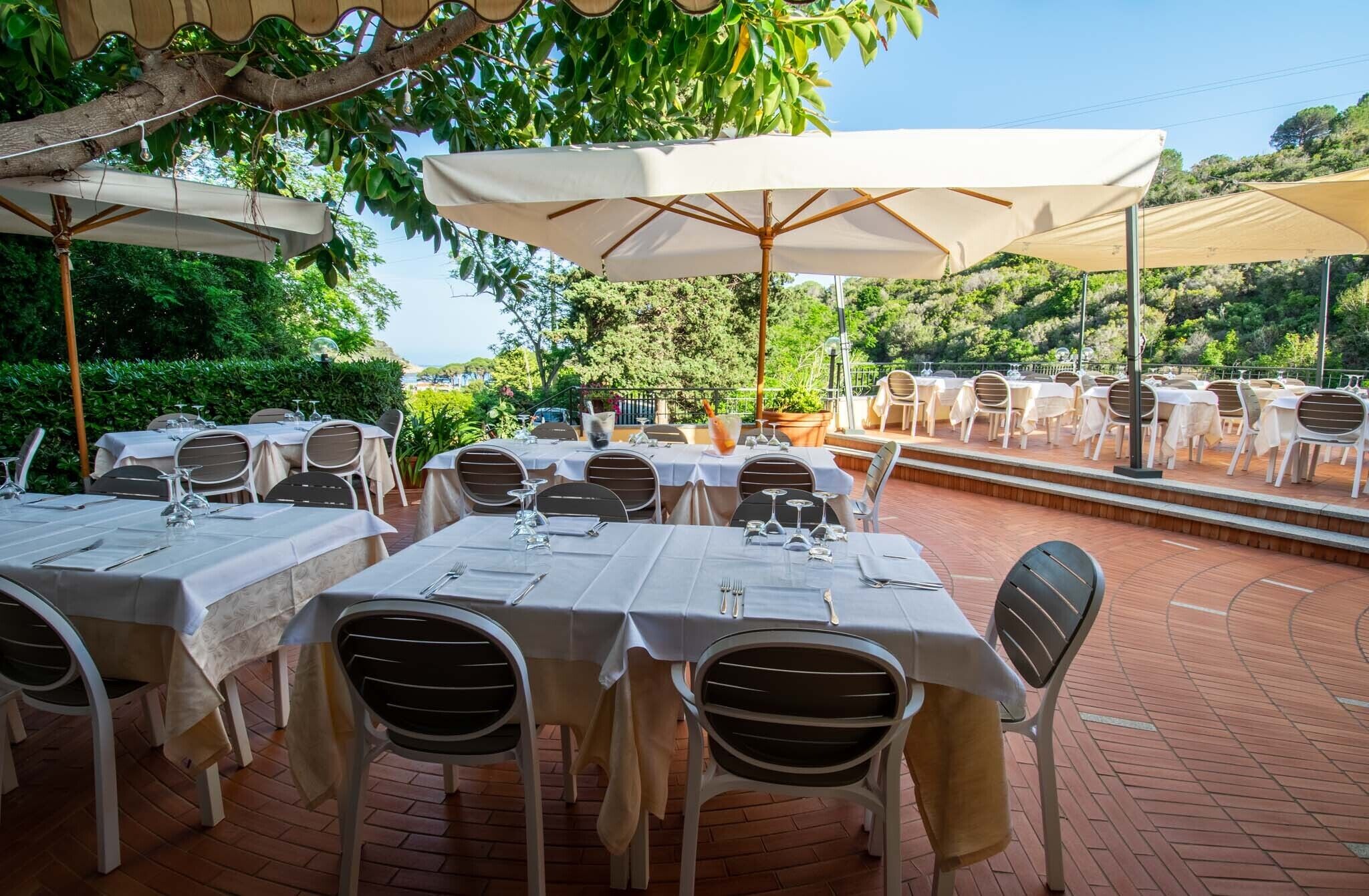 Un restaurante con terraza, mesas cubiertas con manteles blancos y sombrillas que dan sombra.