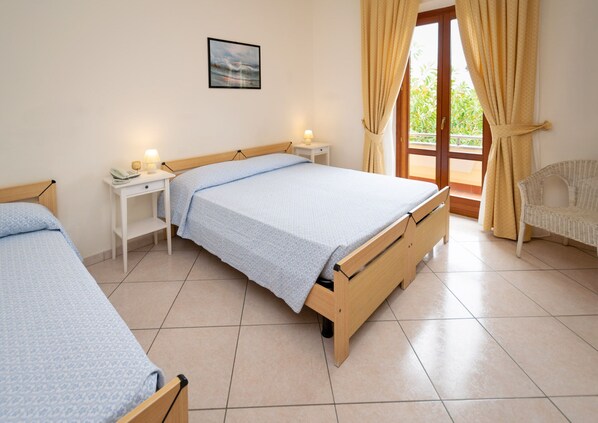 Un dormitorio con dos camas individuales, una mesita de noche con lámpara, una silla y una ventana con cortinas.