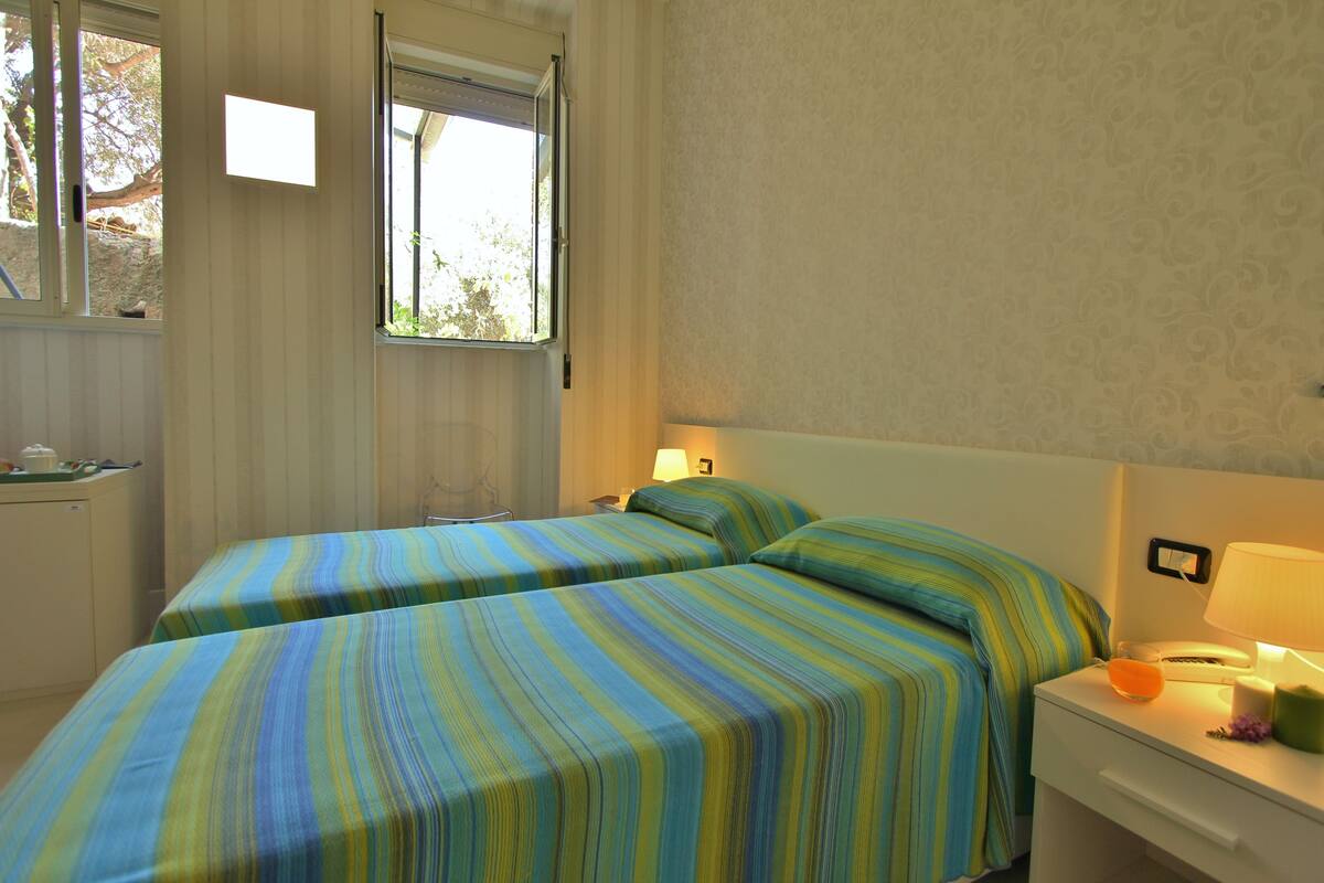 Une chambre avec deux lits, une table de chevet avec une lampe, une fenêtre et un petit bureau avec une chaise.