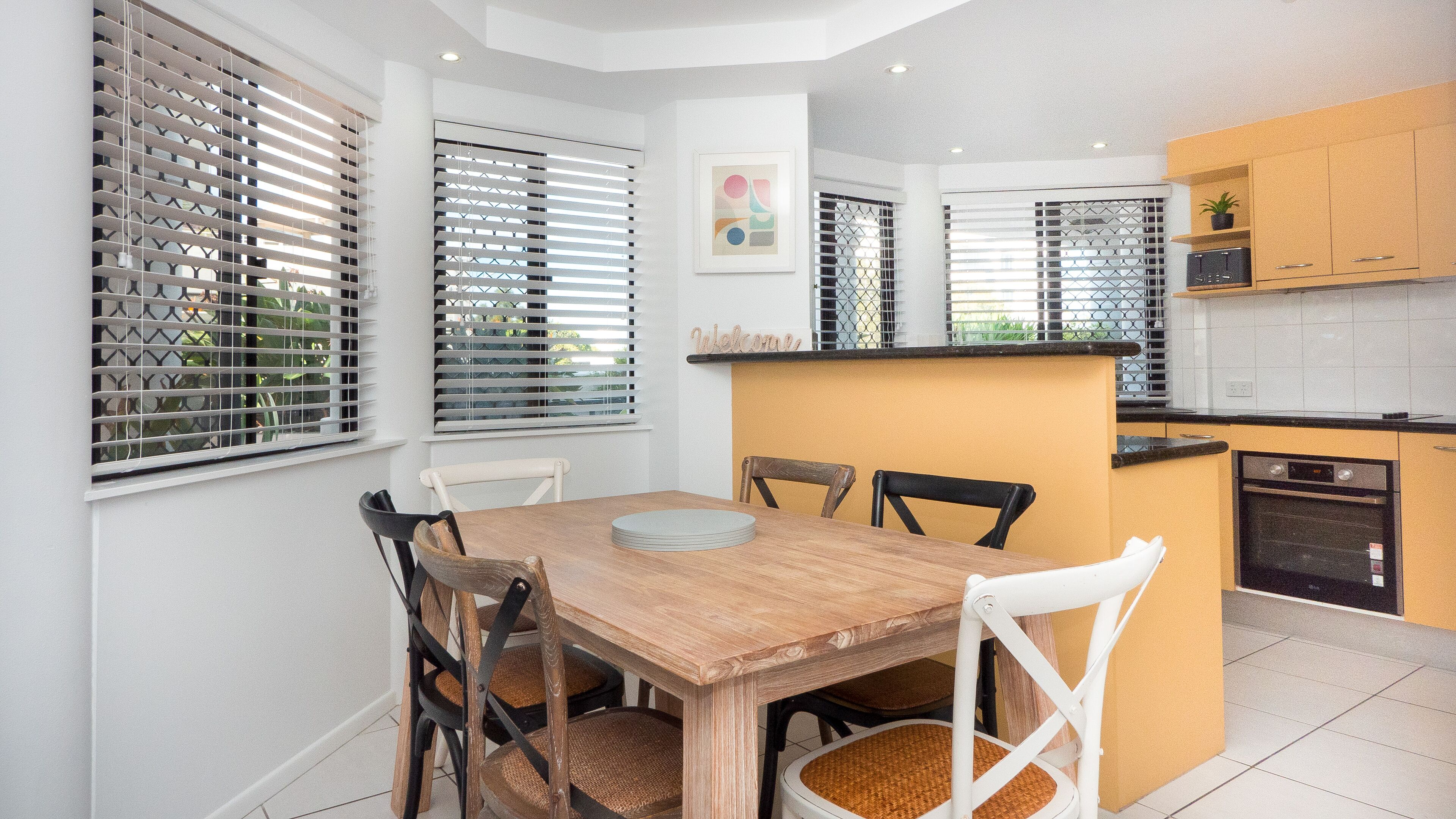 Una cocina moderna con armarios blancos, una mesa de comedor de madera y una pequeña isla con fregadero.