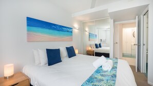 Une chambre d’hôtel avec un grand lit, une table de chevet, une lampe de chevet, un miroir dans la salle de bain et une porte donnant sur une autre pièce.