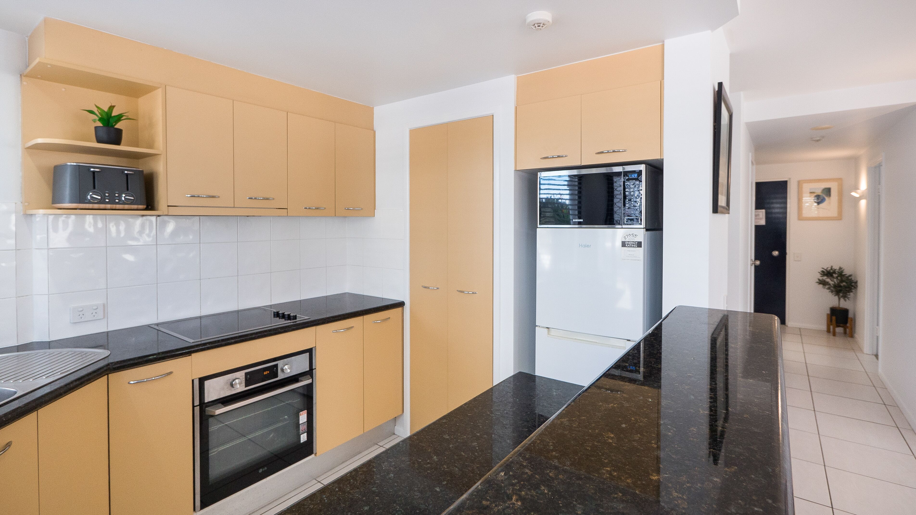 A modern kitchen with wooden cabinets, a black countertop, a built-in oven, and a refrigerator.
