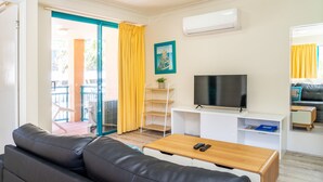 Una sala moderna con un sofá de cuero negro, una mesa de centro de madera, un televisor de pantalla plana y un mueble blanco para equipo audiovisual.