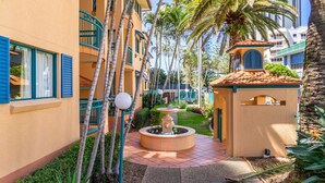 Un patio con una fuente central, palmeras y un pequeño edificio con tejado de baldosas.