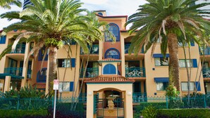 Un hotel con entrada principal, varios balcones y palmeras.