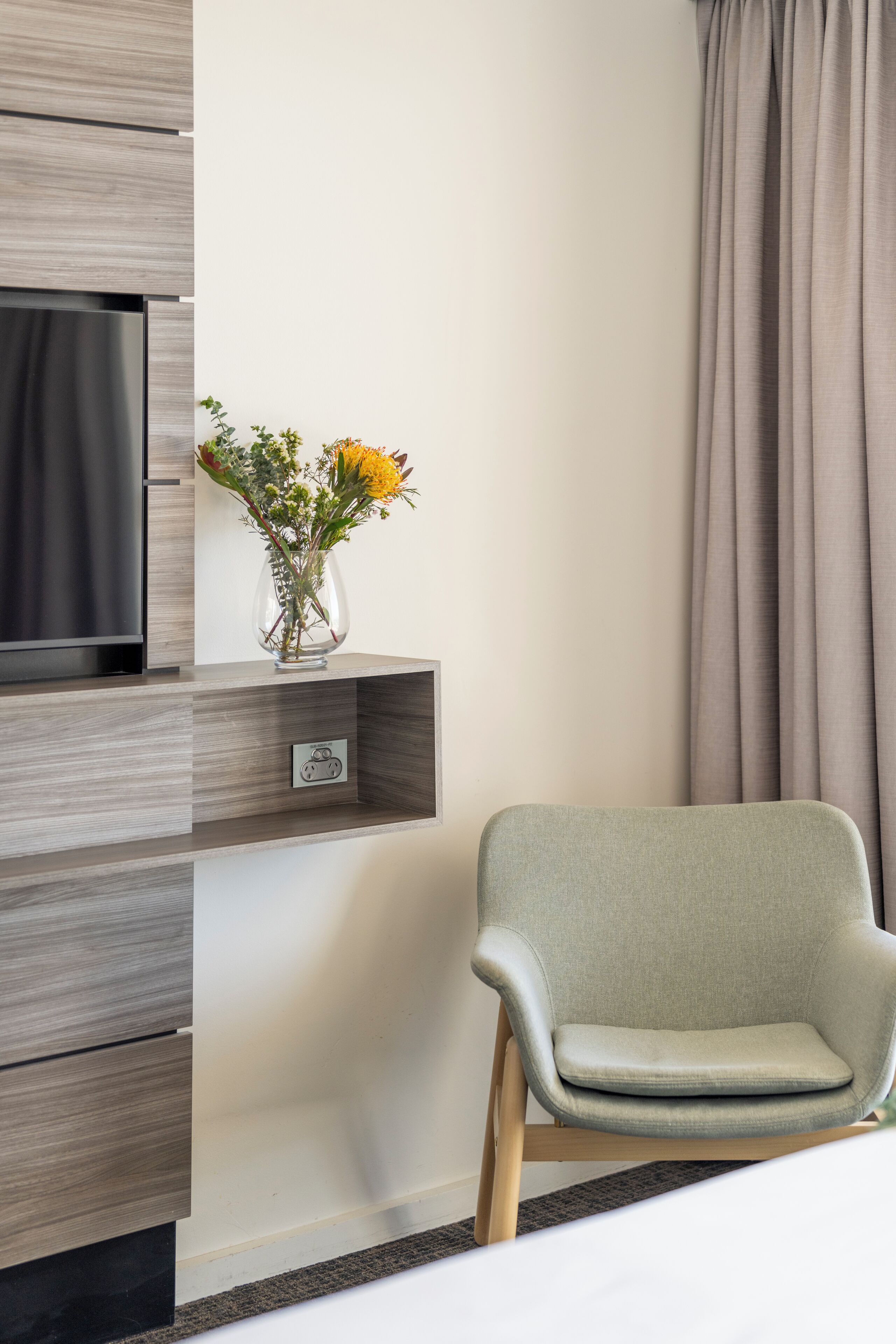 Ein modernes Zimmer mit einem grauen Sofa, einem Fernseher auf einem Holzboden und einer Vase mit Blumen.