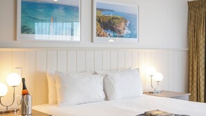 A hotel room with a bed, two framed pictures of coastal scenes, a bottle of champagne, and two bedside lamps. - Ozone Hotel Kangaroo Island (Kingscote)