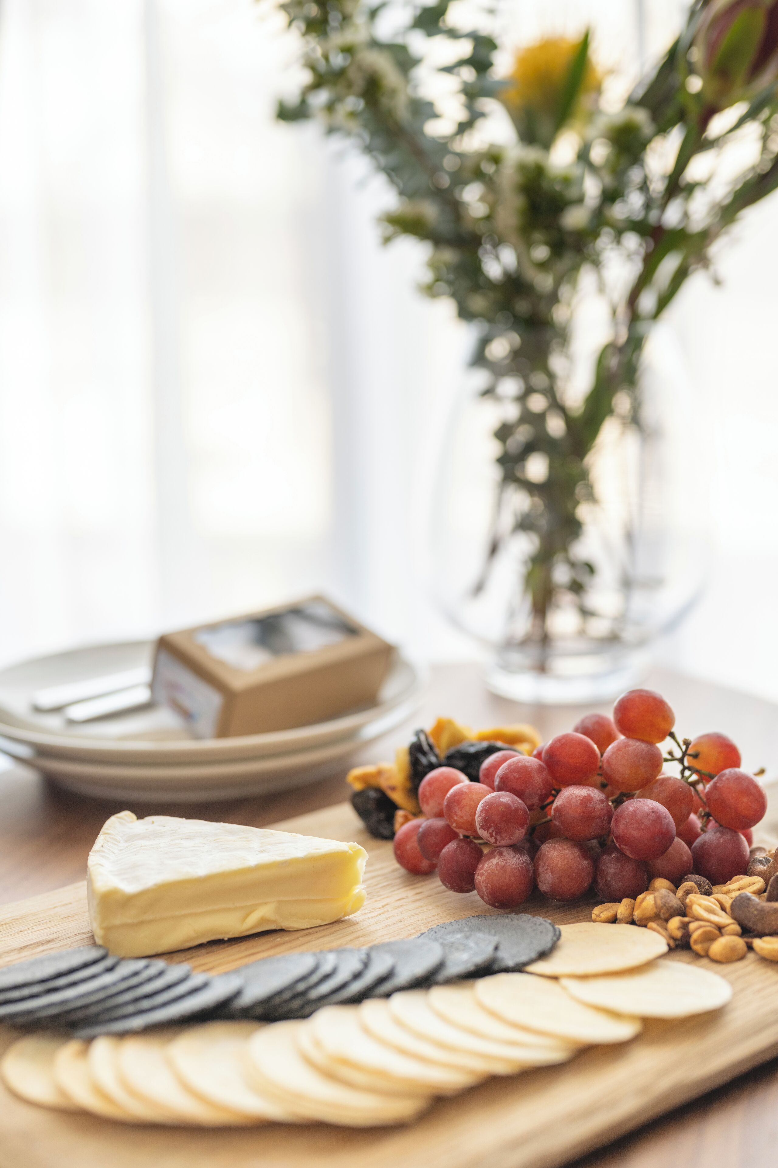 Una tabla de madera con queso, uvas, nueces y galletas.
