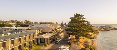 A coastal hotel with a parking lot, a view of the beach, and a row of parked cars.
