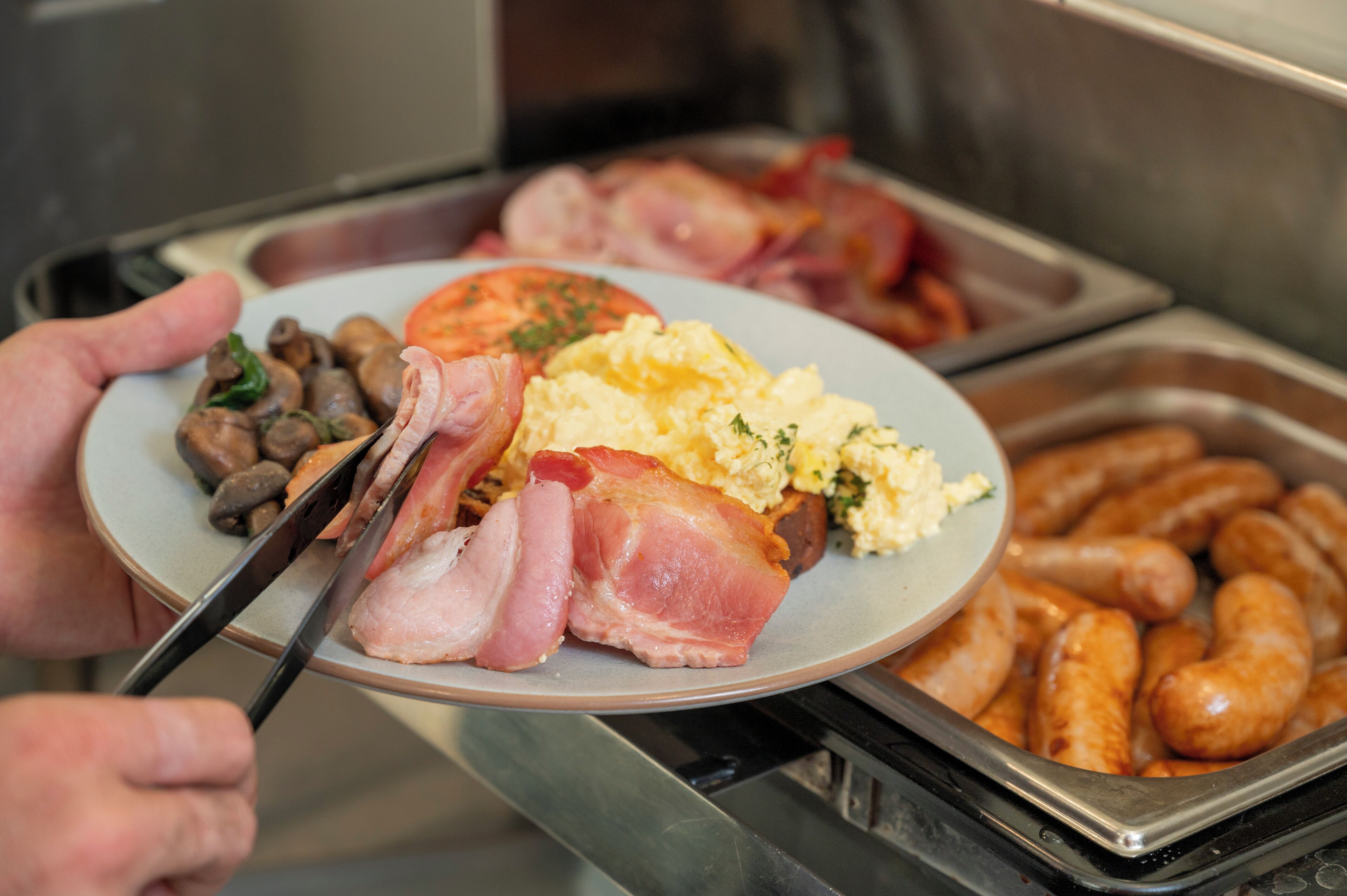 Un bufé con diferentes opciones de comida, incluyendo salchichas, huevos y vegetales.