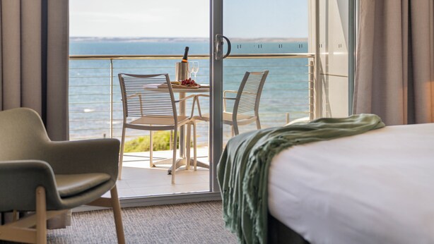 A hotel room with a balcony, a bed, and a table with a bottle and glasses. - Ozone Hotel Kangaroo Island (Kingscote)