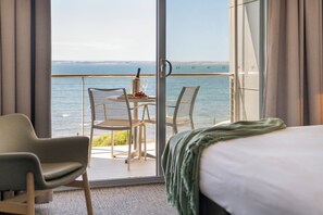 A hotel room with a bed, a chair, a table with a bottle and glasses, and a view of the sea. - Ozone Hotel Kangaroo Island (Kingscote)
