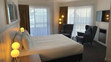 Una habitación de hotel con una cama grande, dos sillones, un televisor de pantalla plana y una chimenea.