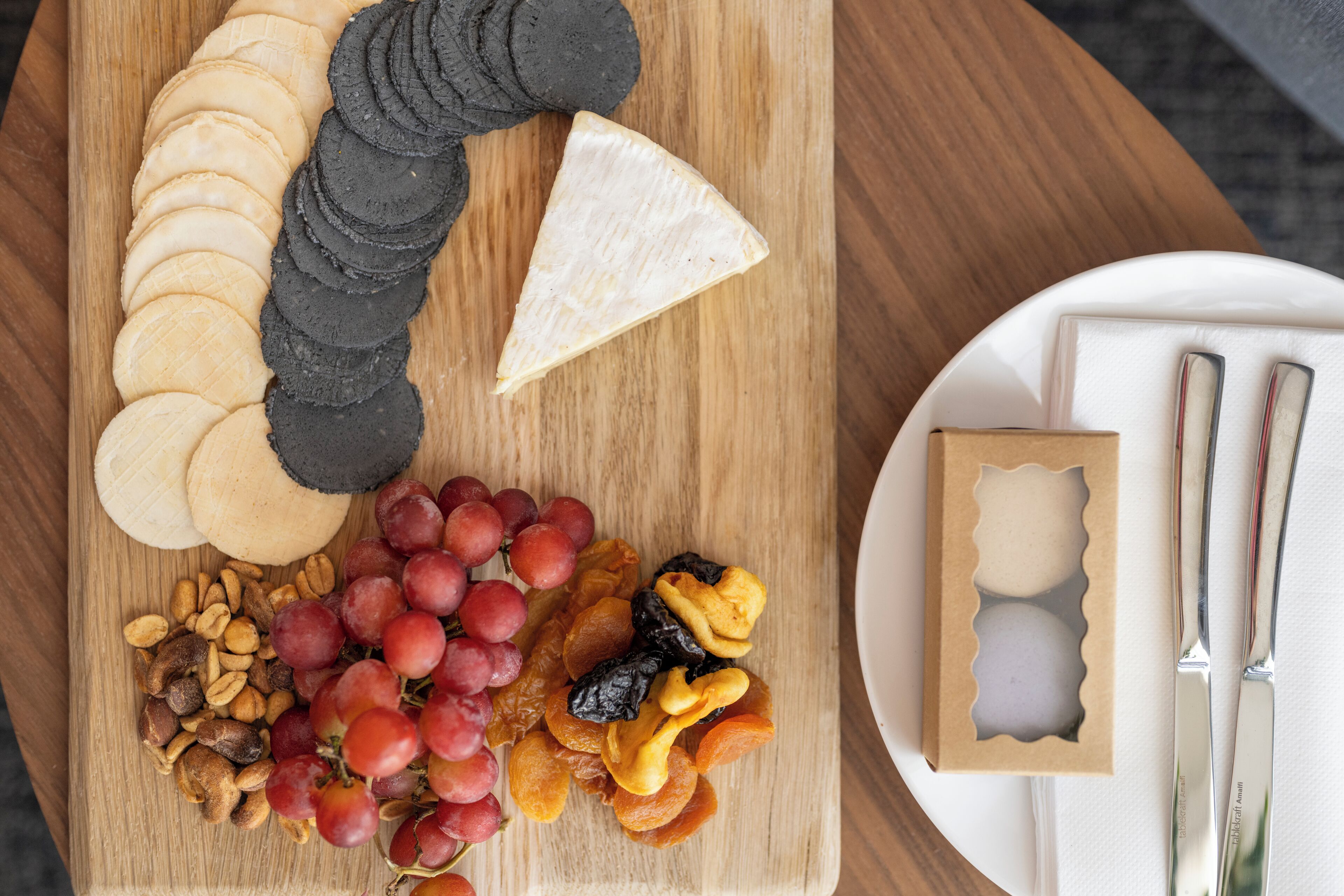 Een houten plank met kaas, crackers, druiven en gedroogd fruit.