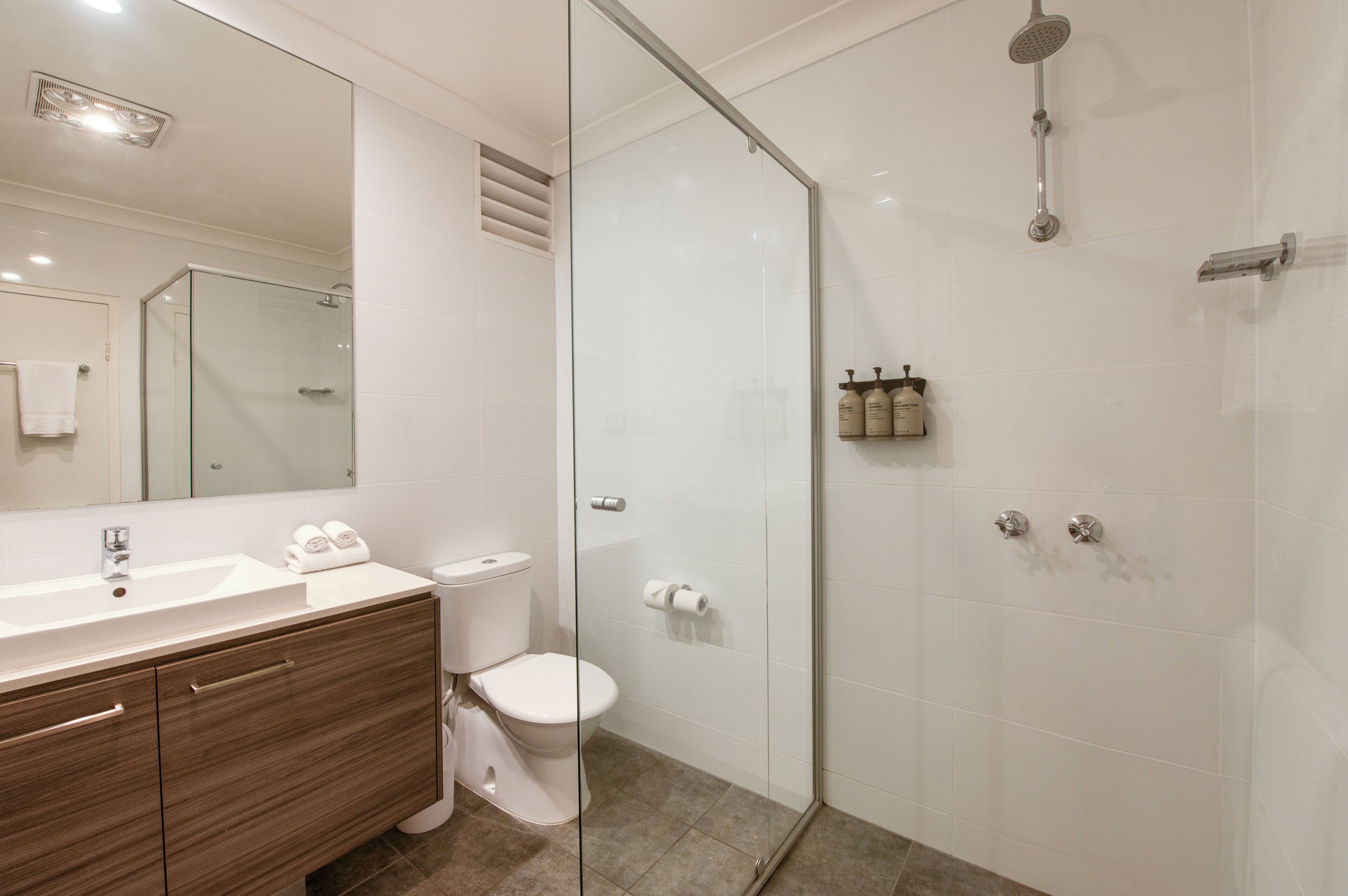 Een moderne badkamer met een glazen douchecabine, een witte wastafel en een houten opbergmeubel.