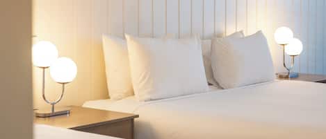 A hotel room with two beds, white bedding, a headboard, bedside tables with lamps, and two framed pictures on the wall.