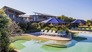 A modern pool area with lounge chairs and umbrellas, surrounded by well-maintained landscaping and a contemporary building. - Serenity Diamond Beach (Diamond Beach)