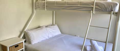 A bunk bed with white bedding and a small bedside table with a basket.