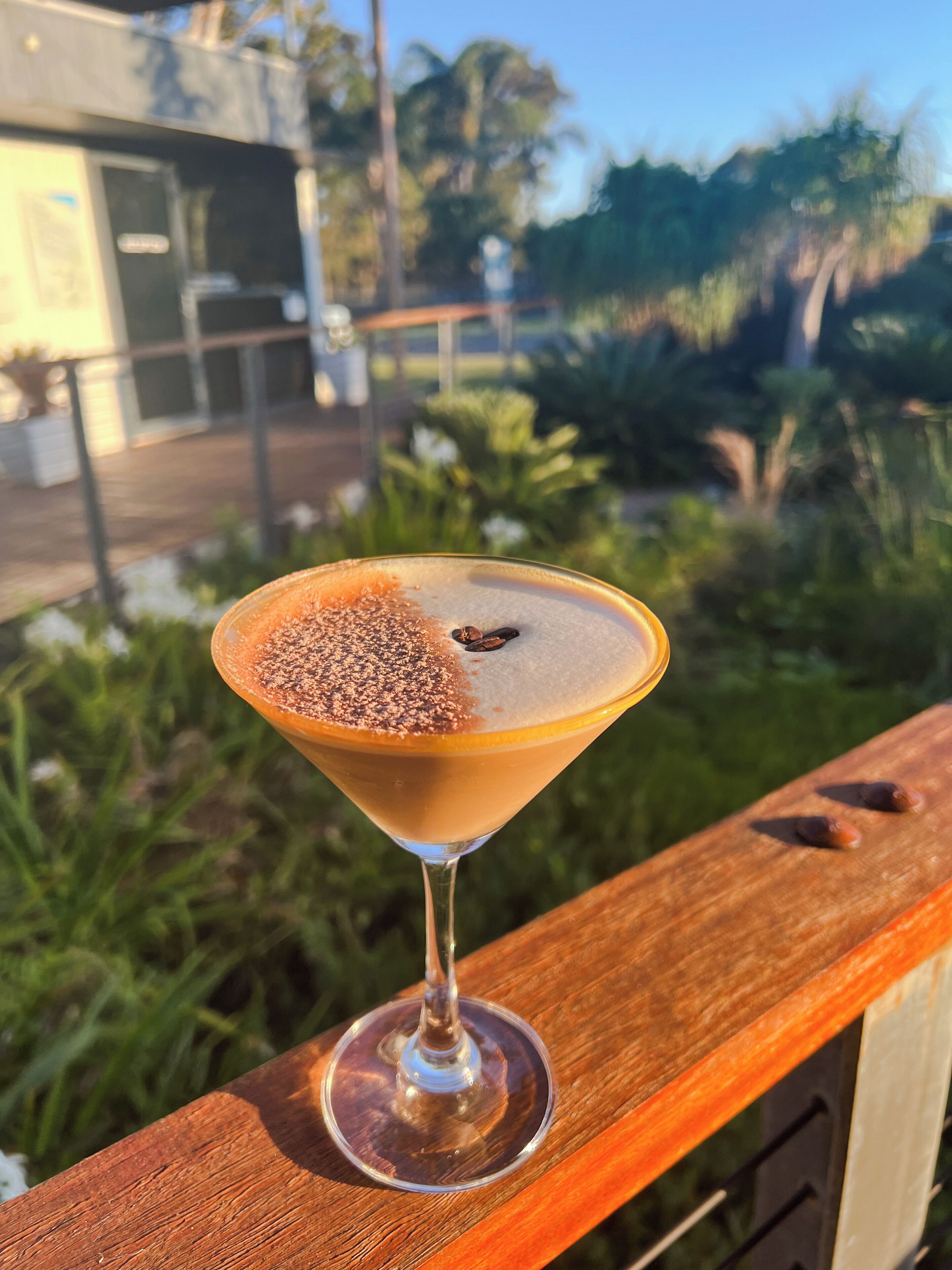 A martini glass with a frothy top, placed on a wooden railing.