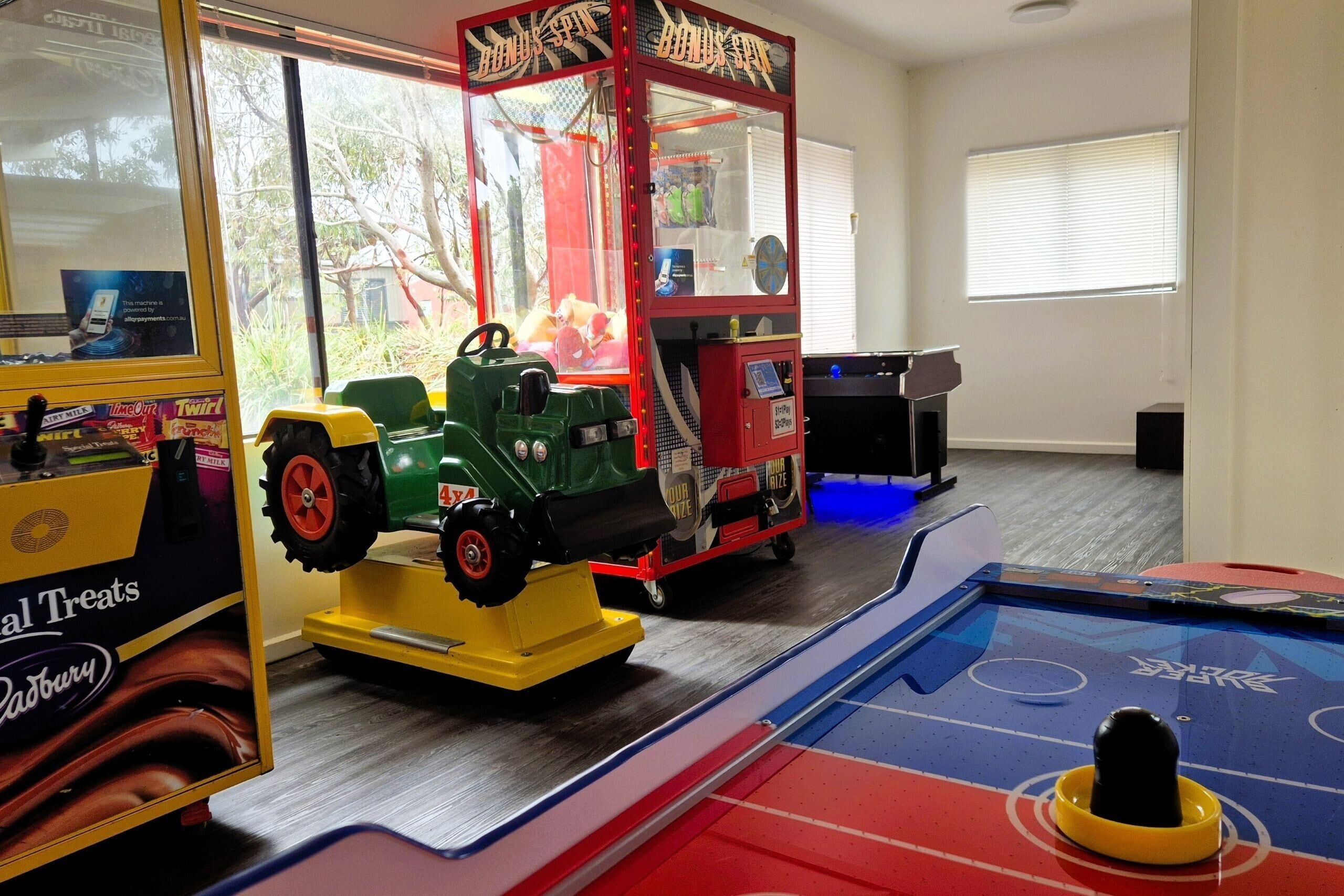 Een kamer met een pooltafel, een tractorspeeltje en een grijpmachine.