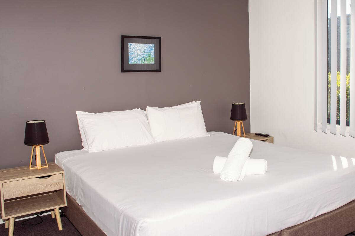 A neatly made bed with white linens, two bedside tables with lamps, and a framed picture on the wall.