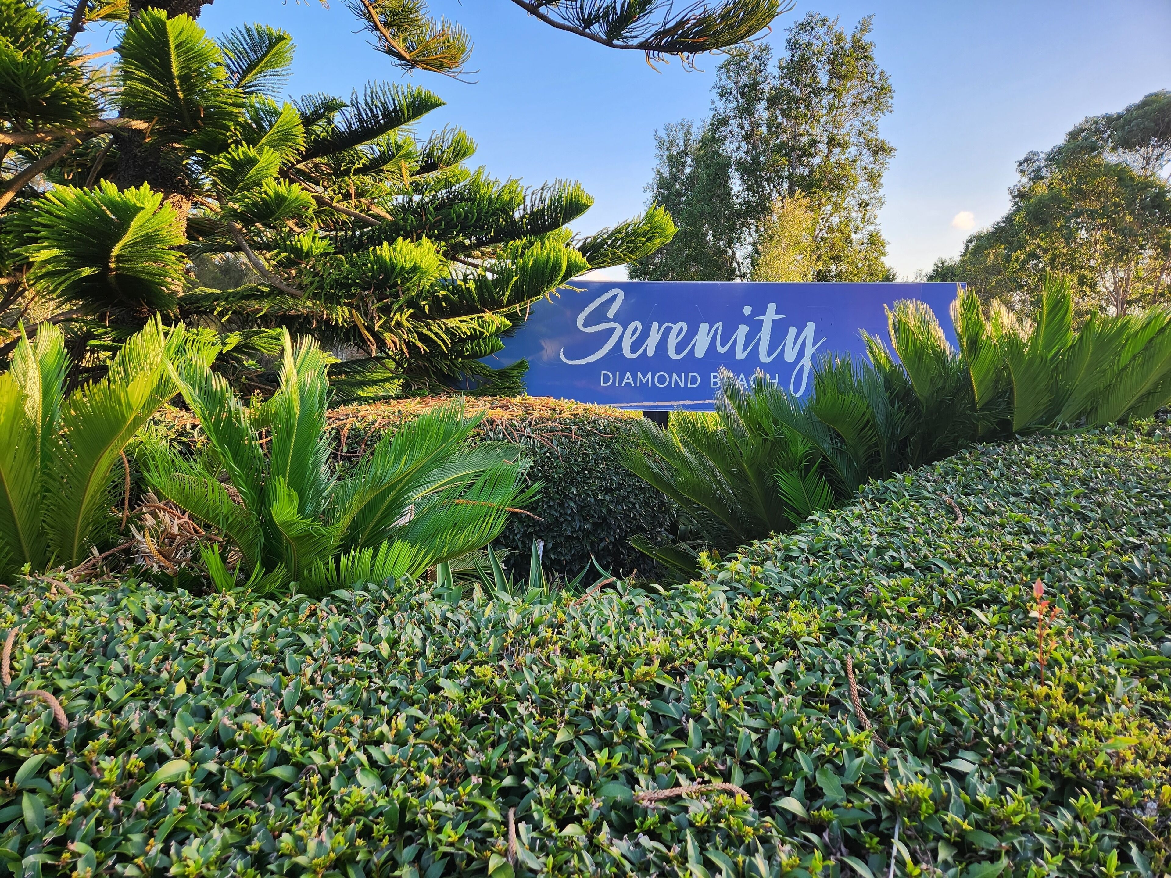 A sign for Serenity Diamond Beach with lush greenery and trees in the background.