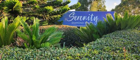 A sign for Serenity Diamond Beach with lush greenery and trees in the background.