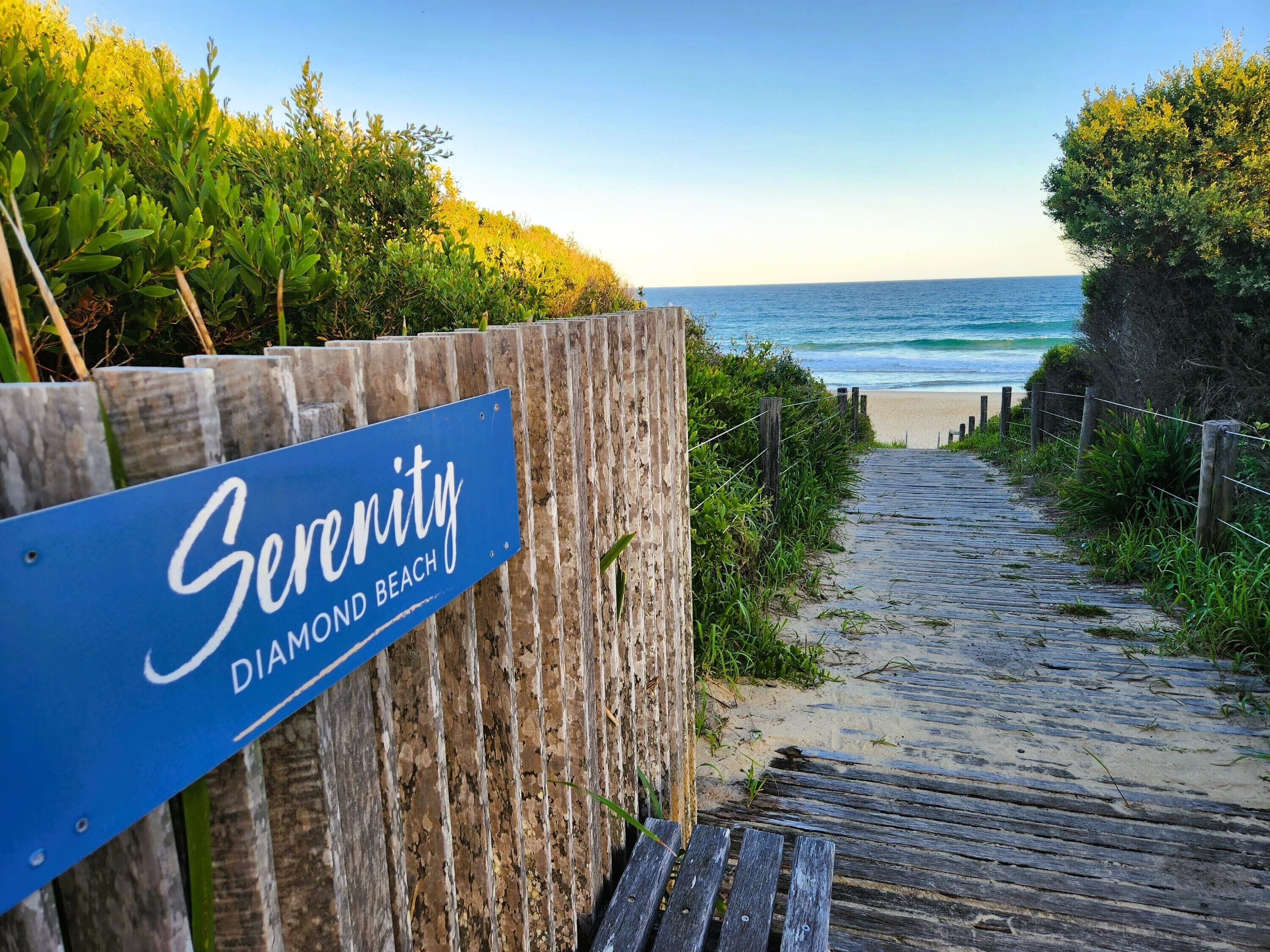 A wooden boardwalk leading to a beach with a sign reading "Serenity Diamond Beach."