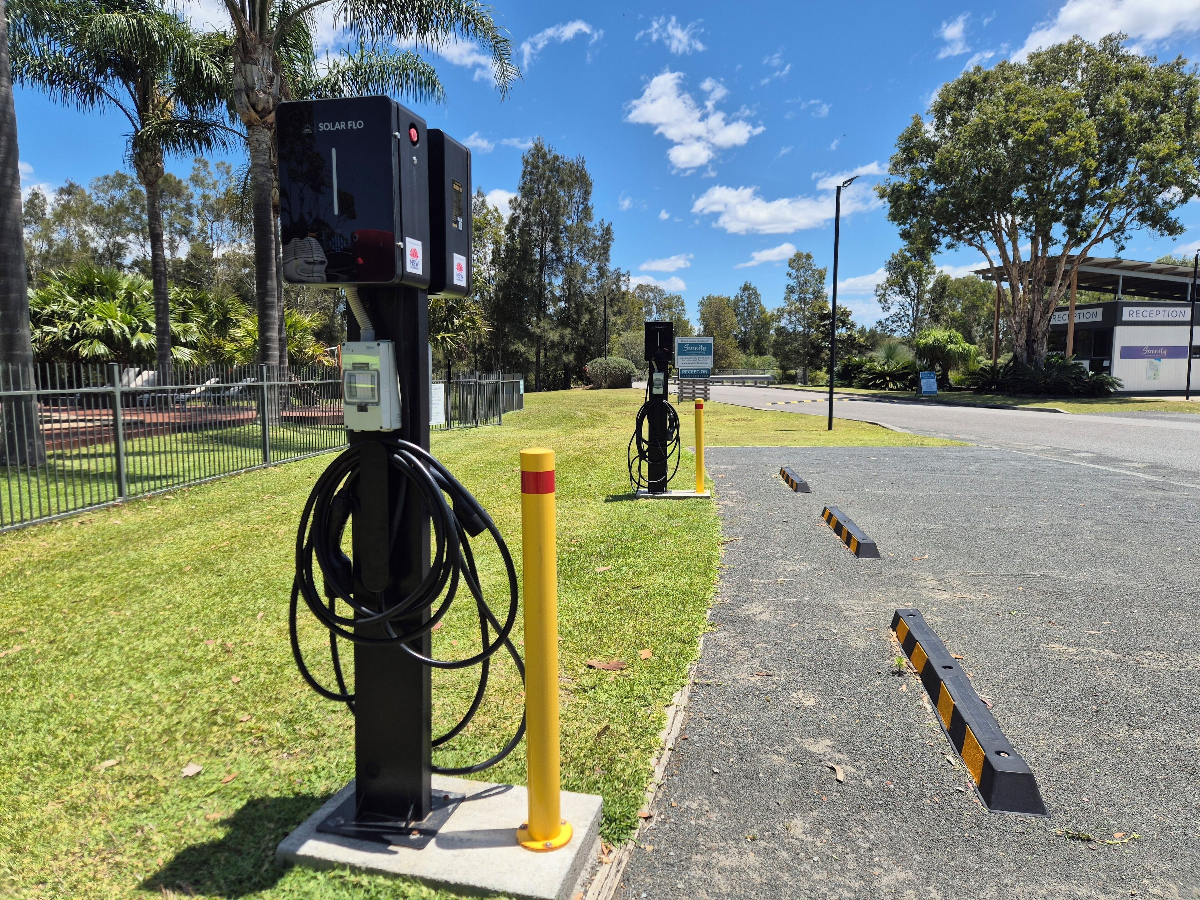 Uma usina de energia solar com uma caixa de controle e uma estação de carregamento em uma área gramada ao lado de uma estrada.