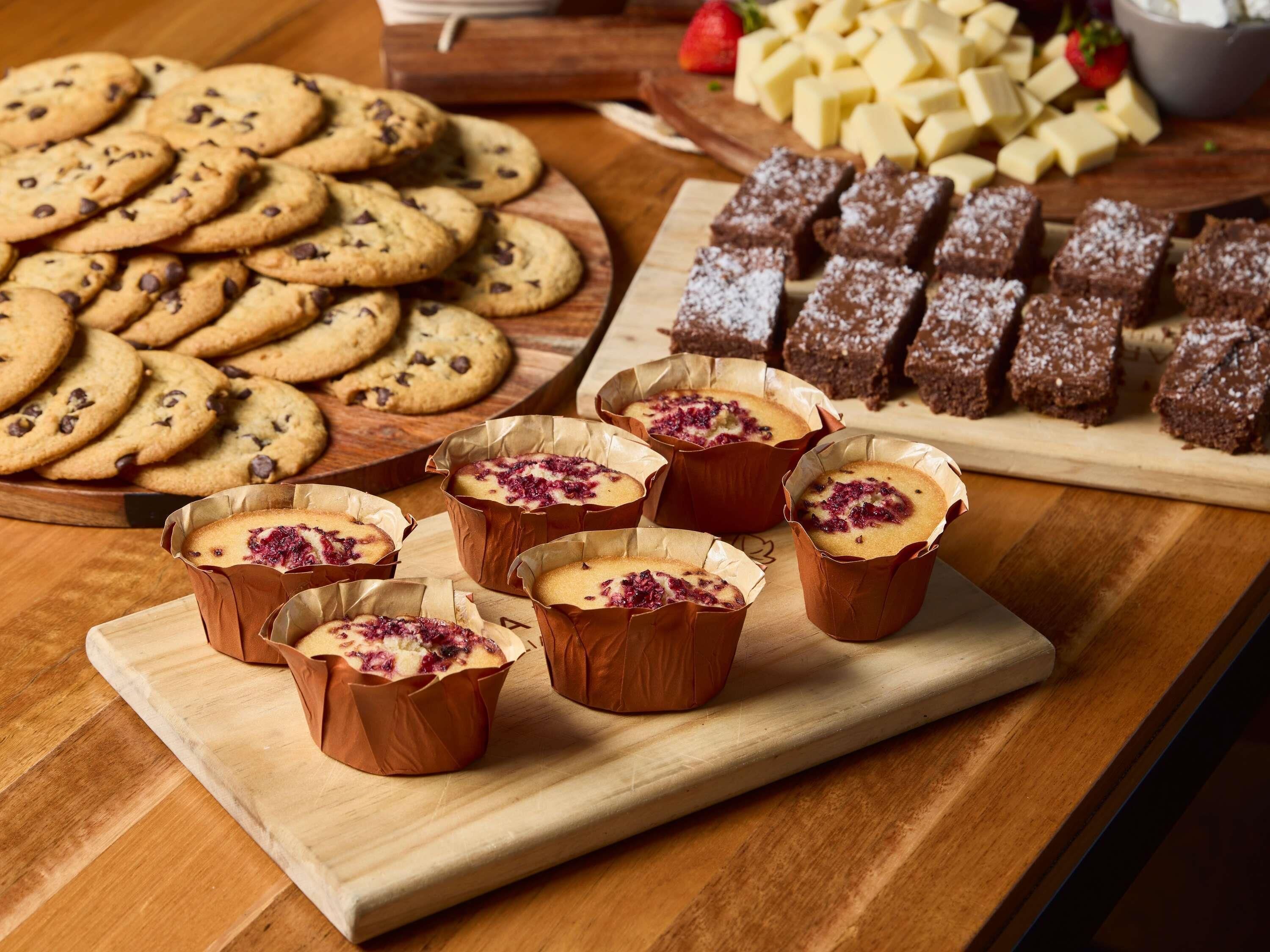 Una mesa de madera con diversas opciones de repostería, como galletas, brownies y muffins.